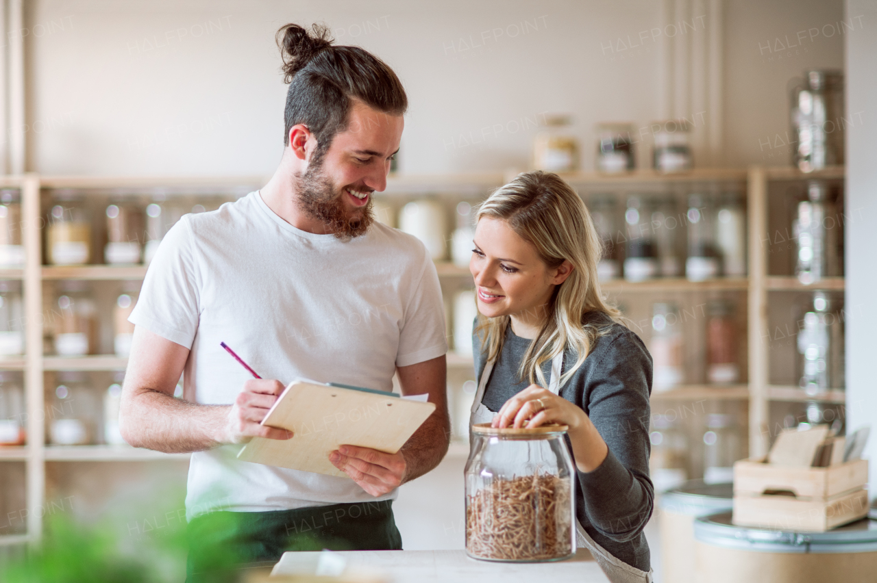 Two shop assistants standing in zero waste shop, checking and ordering stock.