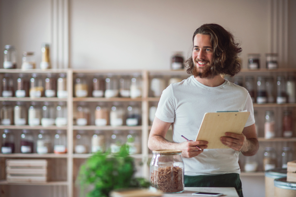 A young male shop assistant standing in zero waste shop, checking stock. Copy space.