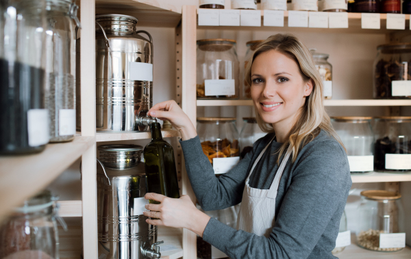 A young female shop assistant in a zero waste shop, filling a bottle with olive oil.