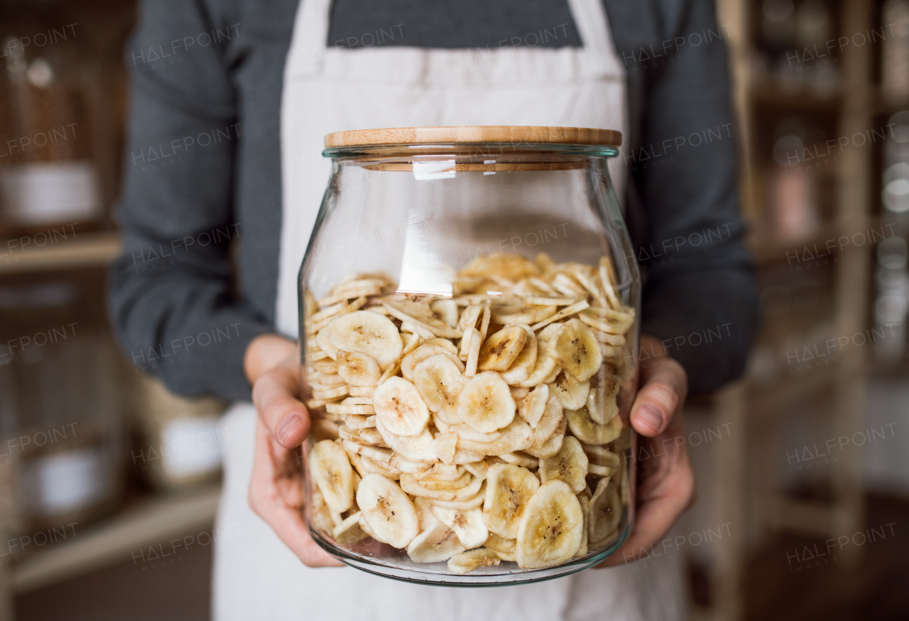 A midsection of a shop assistant in a zero waste shop, holding a jar with groceries. A close-up.