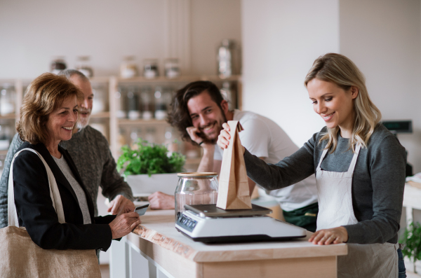 Senior couple customers buying groceries in zero waste shop, sales assistants serving them.