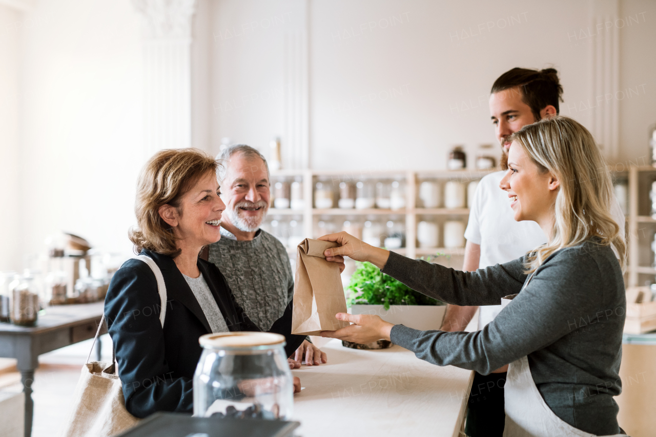 Senior couple customers buying groceries in zero waste shop, sales assistants serving them.