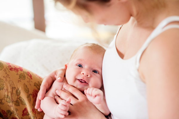 Young mother holding her cute newborn baby son, home bedroom