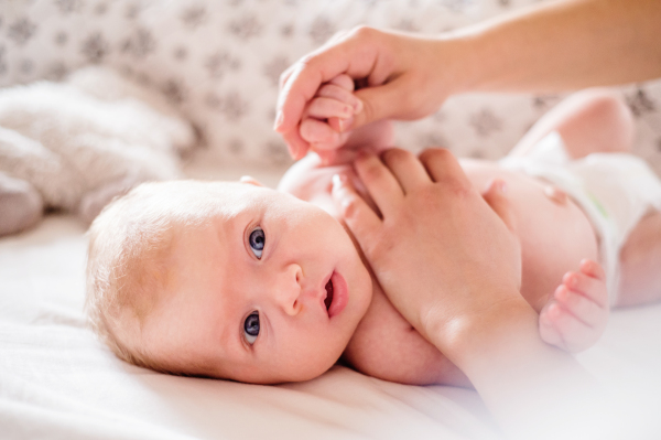 Cute newborn baby boy lying on a bed, held by his mother