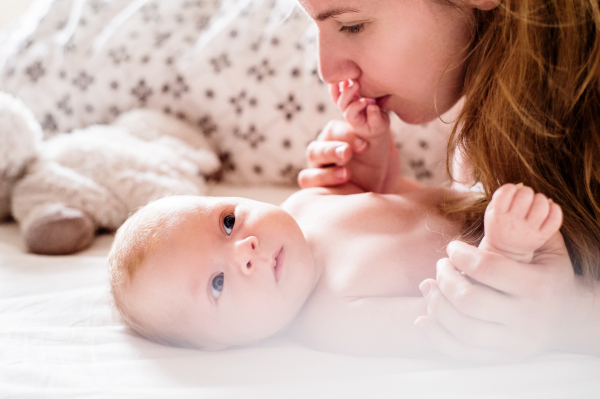 Cute newborn baby boy lying on a bed, held by his mother