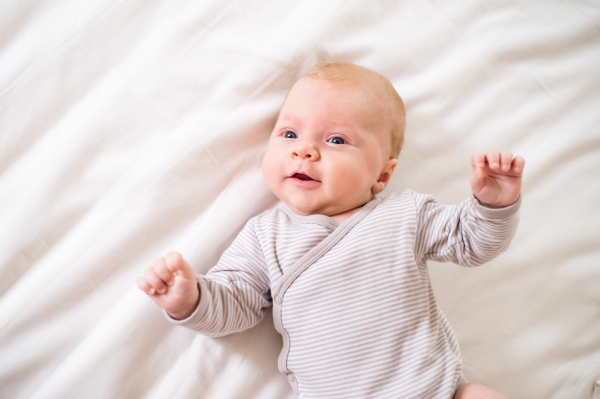 Cute newborn baby boy lying on bed in onesie, white bedroom