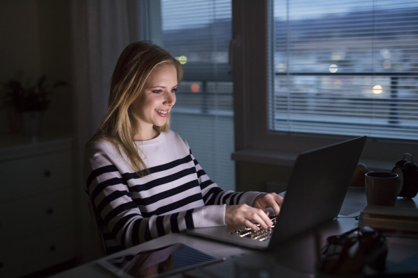 Young beautiful woman sitting at desk, looking at the screen of a laptop late at night.