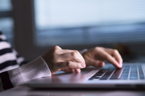 Hands of unrecognizable woman sitting at desk working on laptop late at night. Close up.