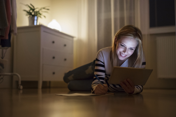 Young beautiful woman lying on the floor, looking at the screen of a tablet late at night.