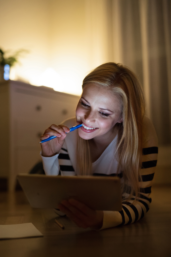 Young beautiful woman lying on the floor, looking at the screen of a tablet late at night.