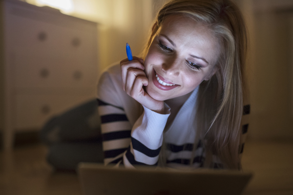 Young beautiful woman lying on the floor, looking at the screen of a tablet late at night.