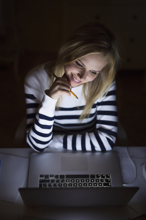 Young beautiful woman sitting at desk, looking at the screen of a laptop late at night.