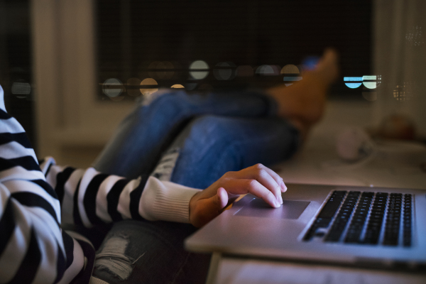 Unrecognizable woman sitting at desk at night working on laptop late at night, legs on table. Close up.