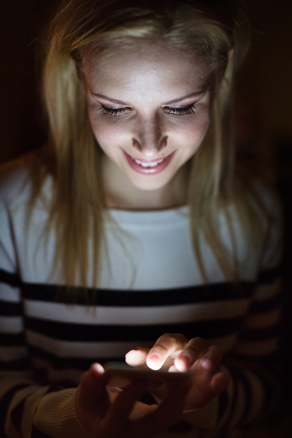 Beautiful young woman sitting at desk at night, holding smart phone, texting.