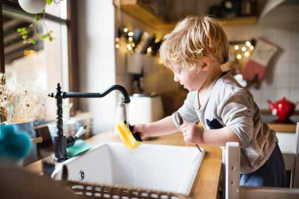 A cute toddler boy washing up the dishes.