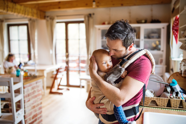 Father with a baby girl in a carrier at home. Paternity leave.