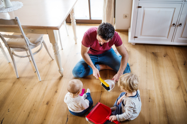 Father and two toddlers with brush and dustpan. Paternity leave. Top view.