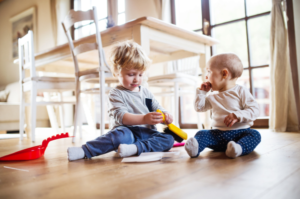 Two toddlers with brush and dustpan sitting on the floor at home.