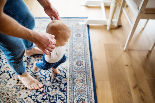 Unrecognizable father with a baby girl at home. First steps. Paternity leave.