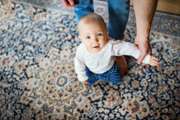 Unrecognizable father with a baby girl at home. First steps. Paternity leave. Top view.