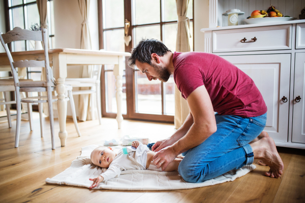 Father changing a baby girl at home. Paternity leave.