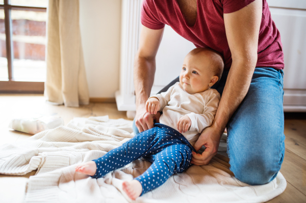 Unrecognizable father with a baby girl at home. Paternity leave.