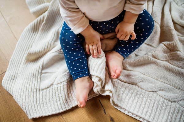 Unrecognizable little toddler at home, sitting on the floor.