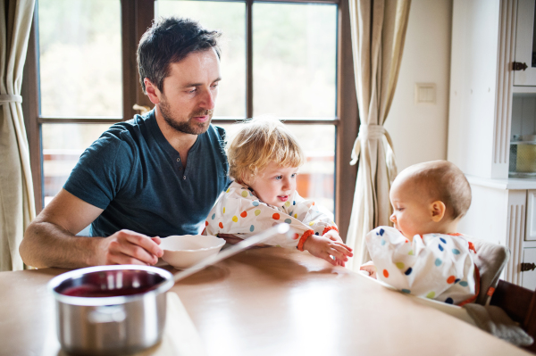 Father feeding two toddlers at home. Paternity leave.