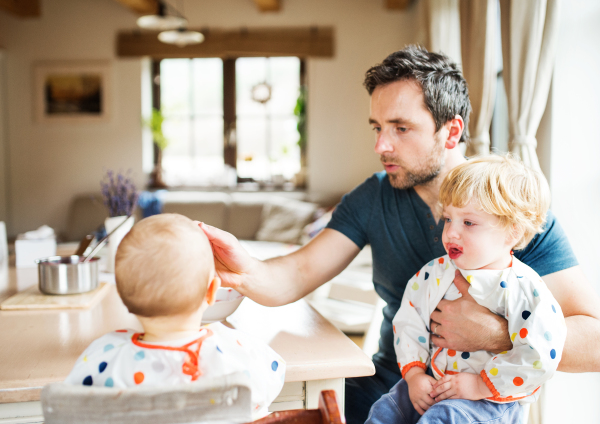 Father feeding two toddlers at home. Paternity leave.