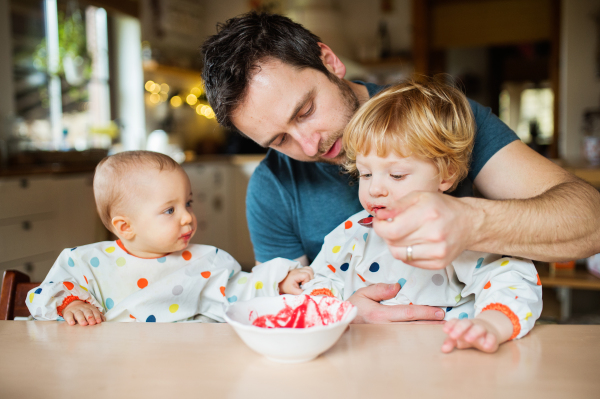 Father feeding two toddlers at home. Paternity leave.