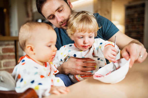 Father feeding two toddlers at home. Paternity leave.