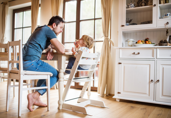 Father sitting at the table with a toddler boy at home. Paternity leave.