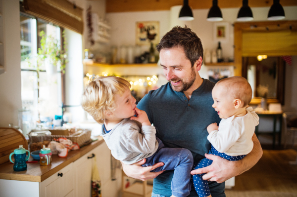 Father holding two toddlers at home. Paternity leave.