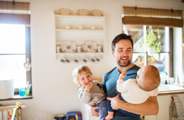 Father holding two toddlers at home. Paternity leave.