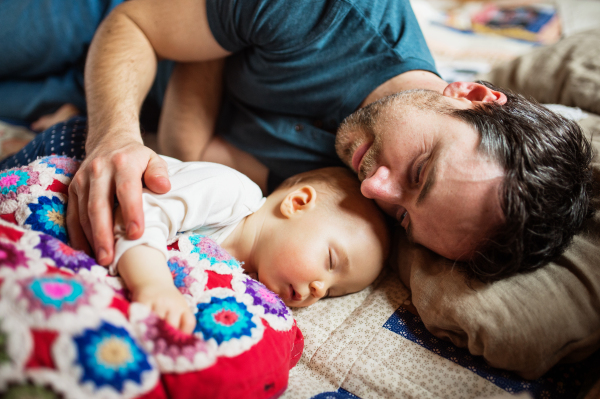 Father with a baby girl at home, sleeping on the sofa. Paternity leave.