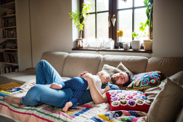 Father with a baby girl at home, sleeping on the sofa. Paternity leave.