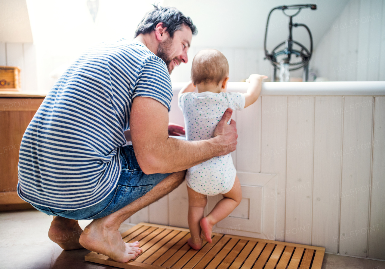 Father with a toddler child at home standing by the tub in the bathroom. Paternity leave.