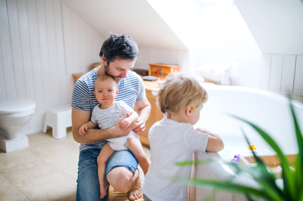 Father with two toddlers getting ready for the bath in the bathroom at home. Paternity leave.