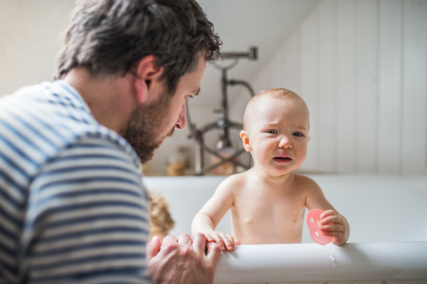 Father washing two toddlers in the bath in the bathroom at home. Paternity leave.