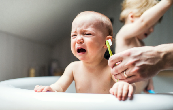 Father washing two toddlers in the bath in the bathroom at home. Paternity leave. An unhappy baby girl crying when brushing teeth.