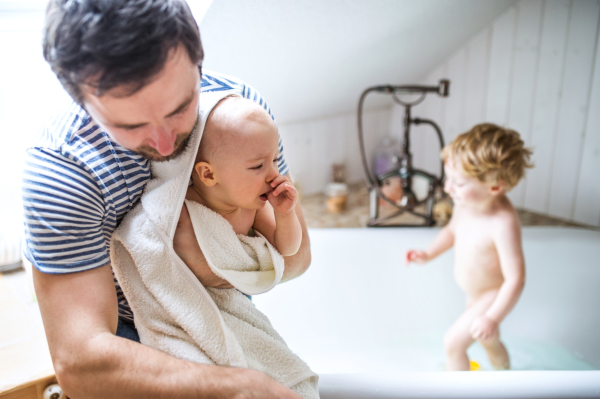 Father washing two toddlers in the bath in the bathroom at home. Paternity leave.