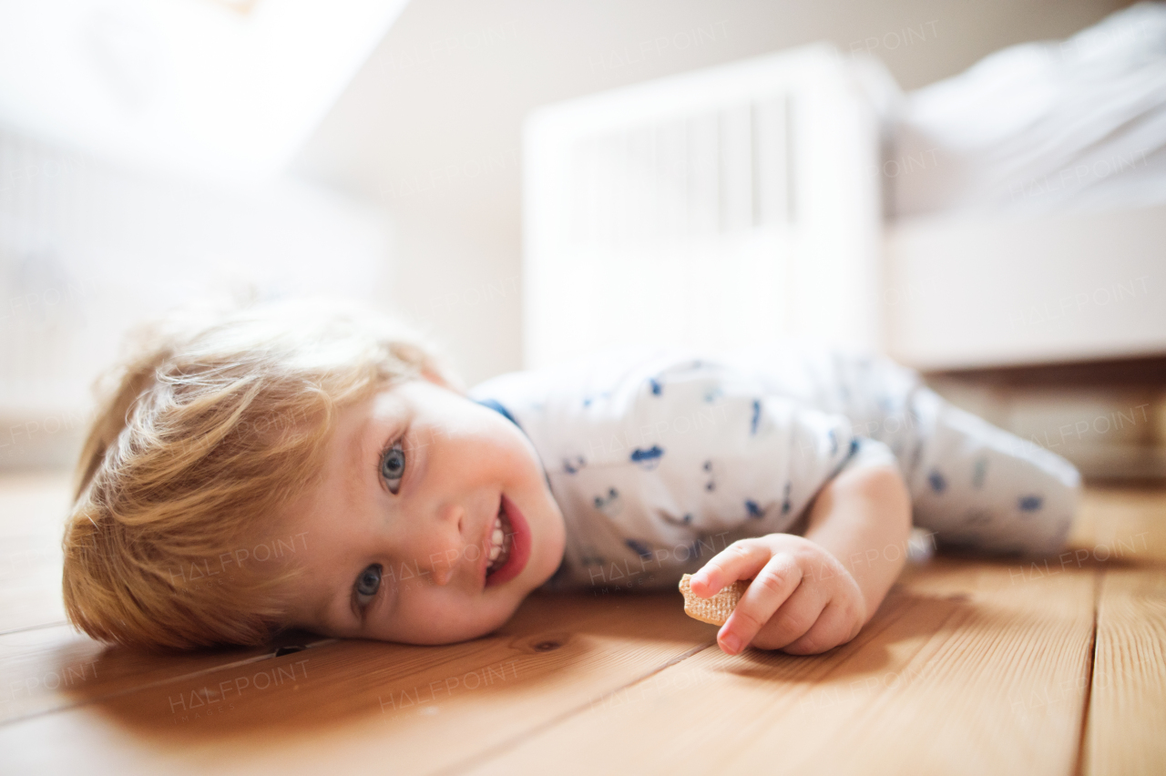 A happy toddler boy in the bedroom at home, lying on the floor and holding biscuit.