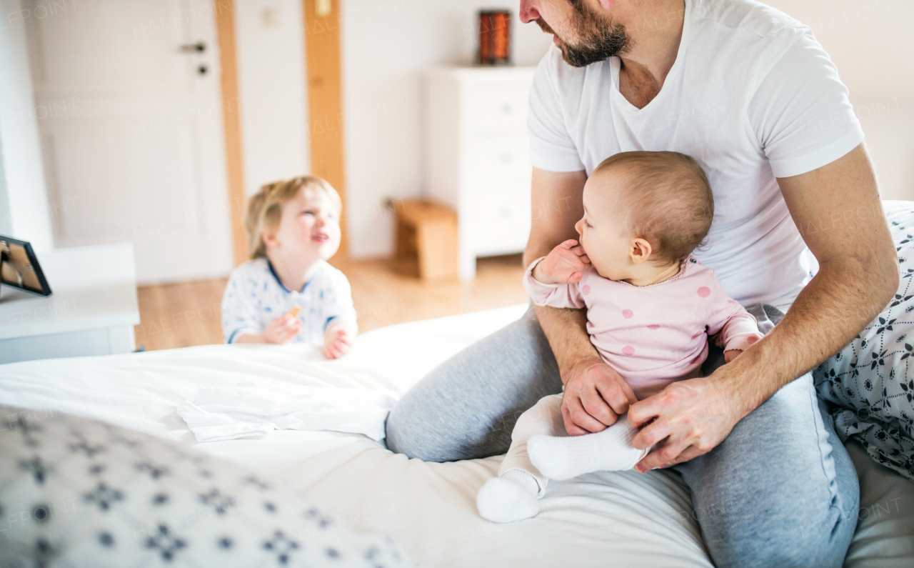 Unrecognizable father with toddler children in bedroom at home at bedtime. Paternity leave.