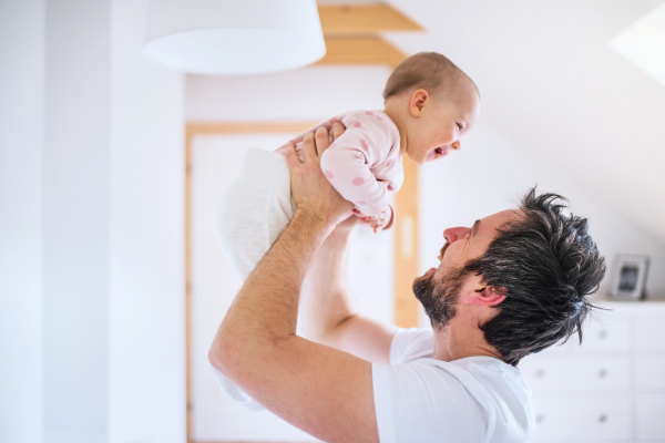 Father holding up a toddler girl in bedroom at home, having fun. Paternity leave.