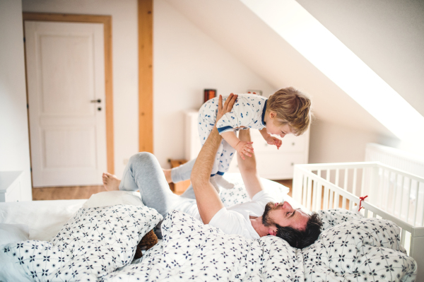 Mature father with a toddler boy having fun in bedroom at home at bedtime. Paternity leave.