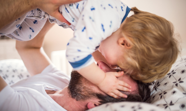 Mature father with a toddler boy having fun in bedroom at home at bedtime. Paternity leave. Close up.