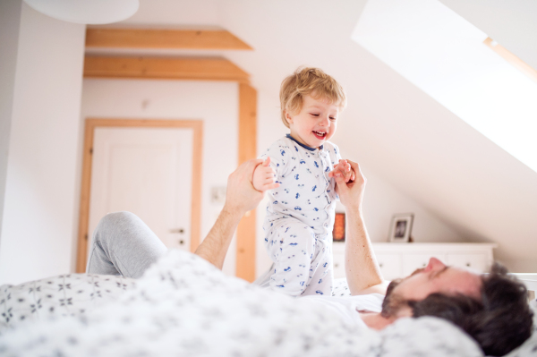 Mature father with a toddler boy having fun in bedroom at home at bedtime. Paternity leave.