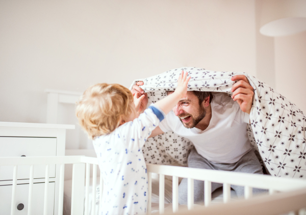 Father with a toddler boy having fun in bedroom at home at bedtime. Paternity leave.