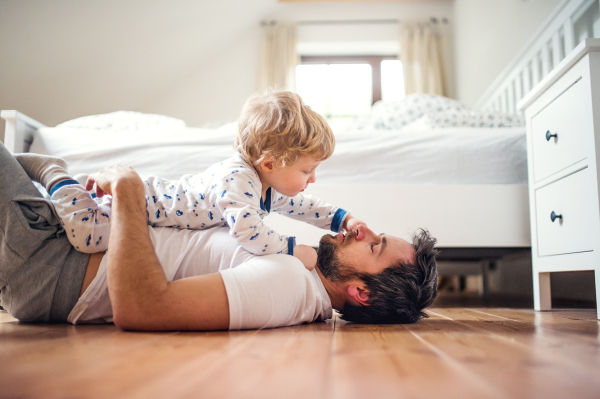 Mature father with a toddler boy having fun in bedroom at home at bedtime. Paternity leave.