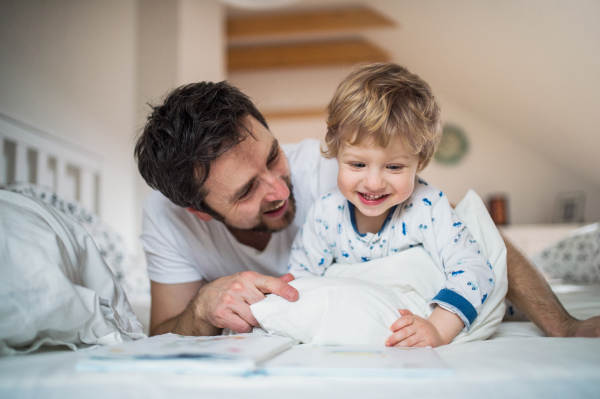 Mature father with toddler boy in bedroom at home, reading stories at bedtime. Paternity leave.